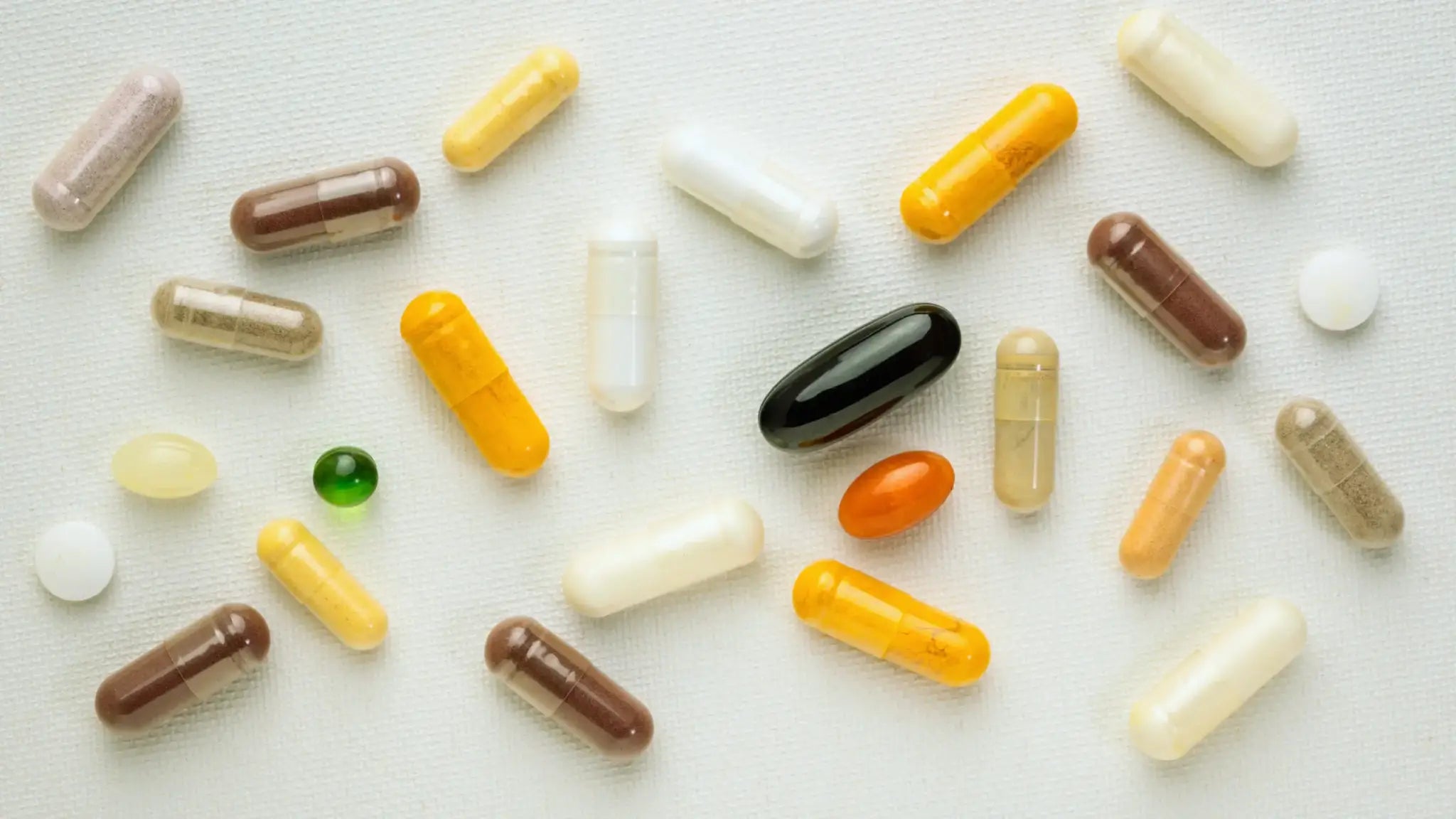Assorted yellow, brown, and white supplement capsules scattered on a white surface, representing a comparison between NADH and NAD+ supplements.