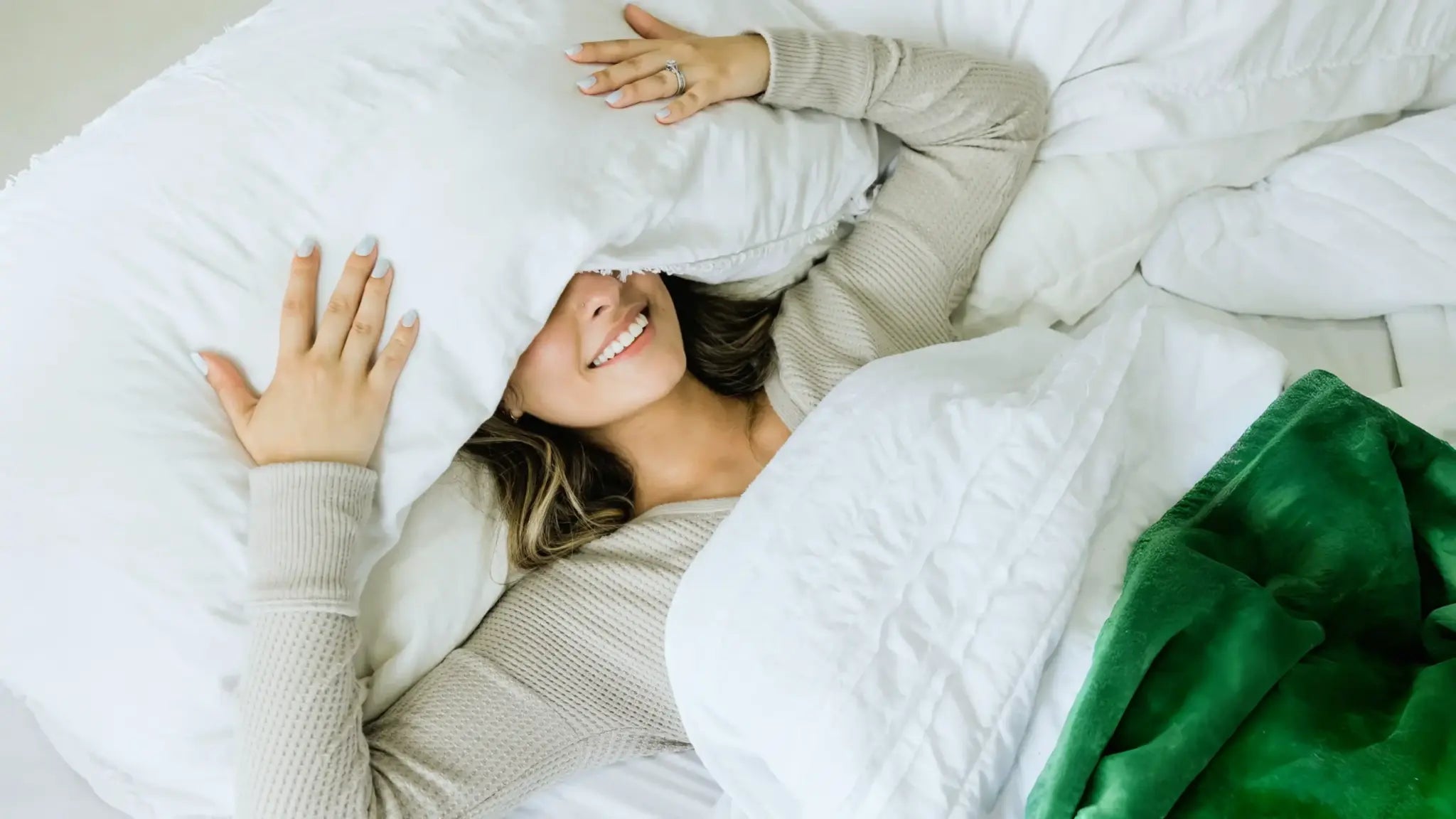 Smiling woman lying in bed with a pillow over her head, illustrating restful sleep and the calming benefits of apigenin for healthy aging.