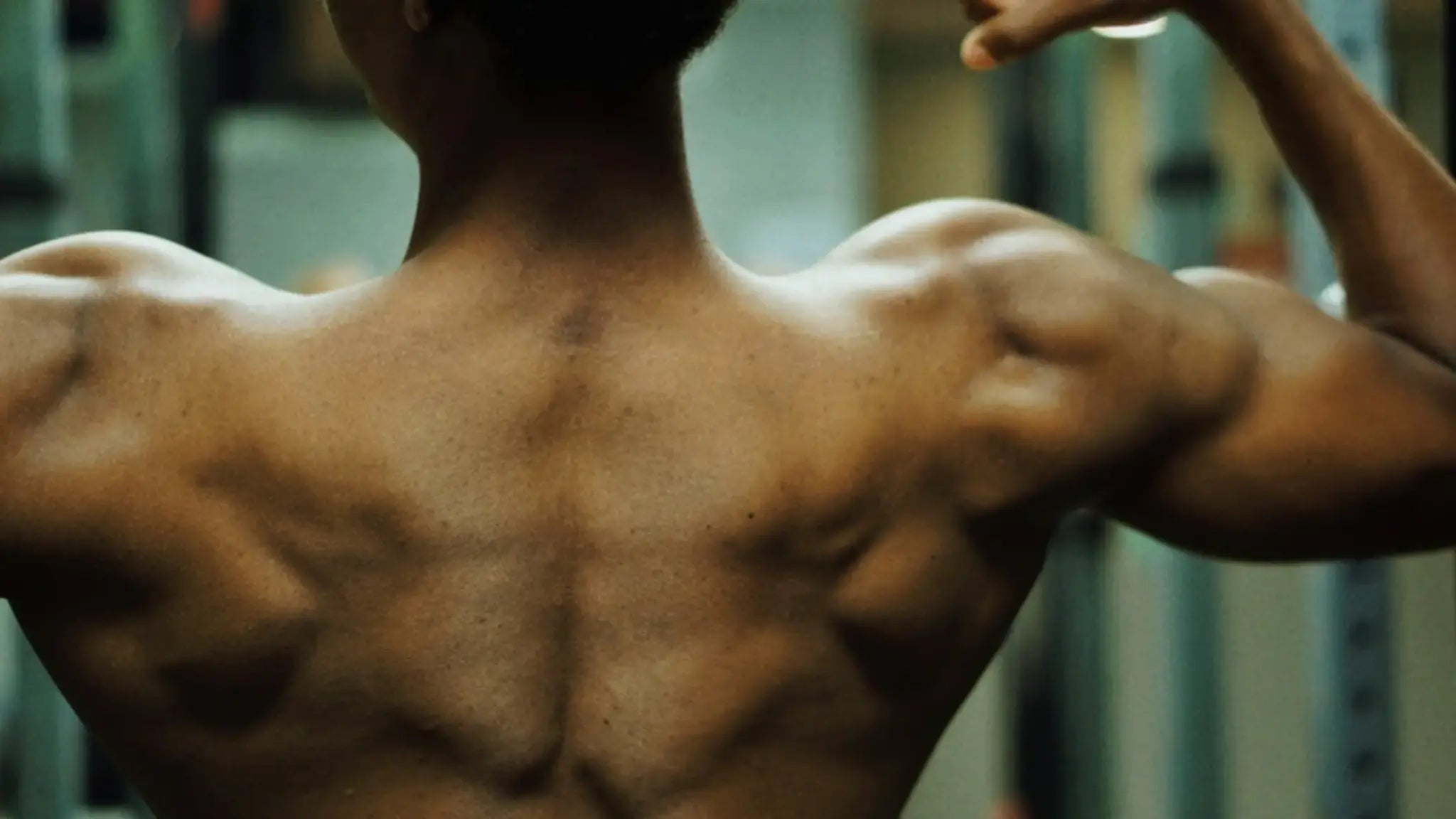 Muscular person flexing their back and shoulders in a gym setting, symbolizing strength and performance benefits of AKG supplements.