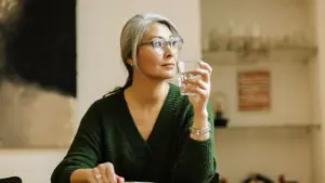 middle aged woman drinking water and looking through the window