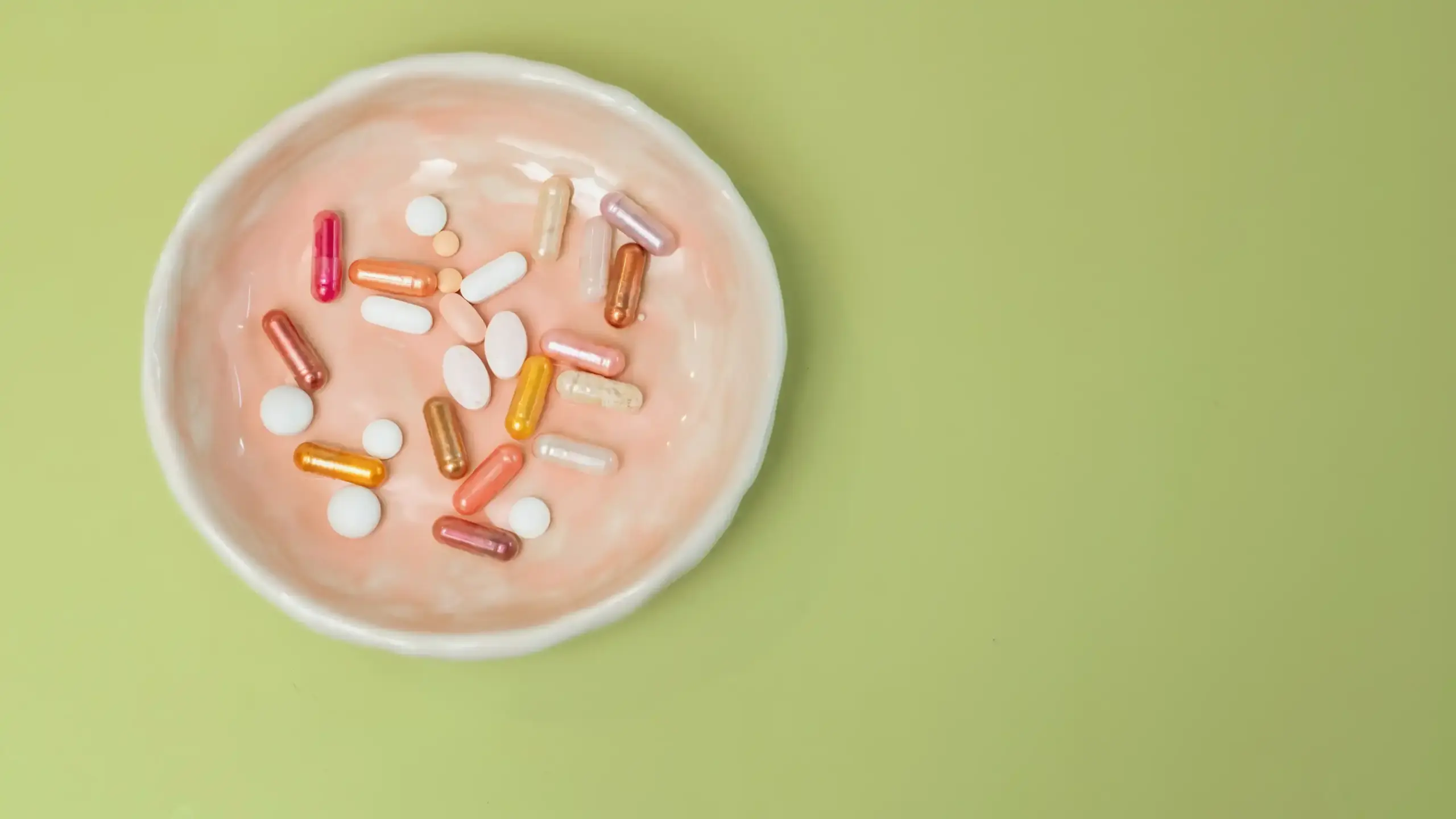 A pink bowl filled with an assortment of colorful supplement capsules.