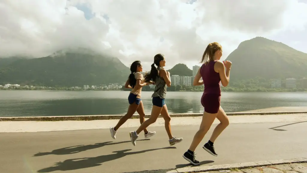 Three women running along a lakeside trail, with stunning mountains in the background