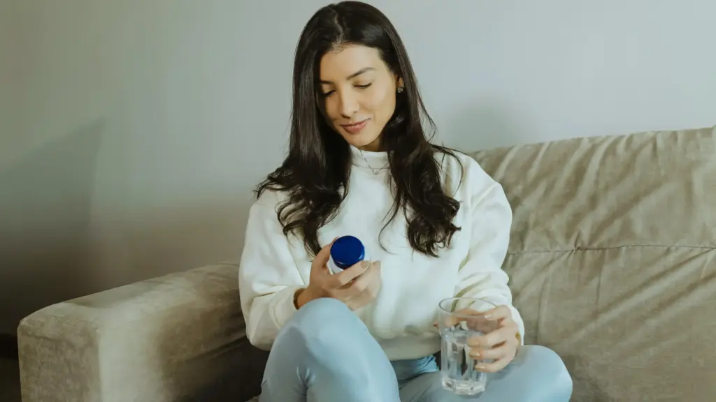 Woman sitting on a couch, examining the label on a supplement bottle.