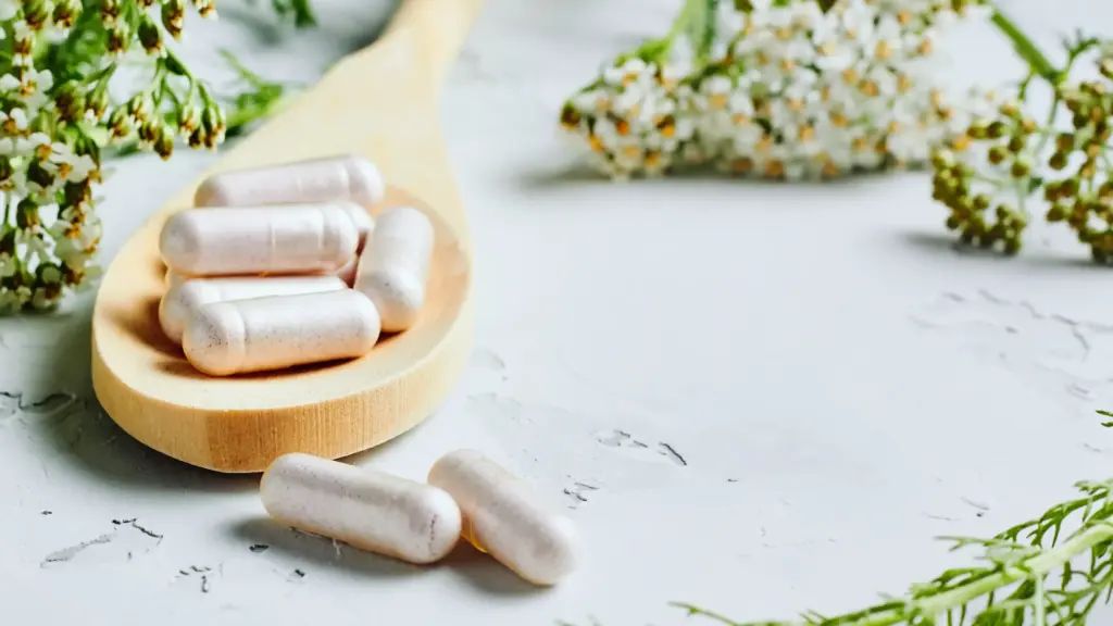 A close-up of supplement capsules resting on a wooden spoon, set against a neutral background