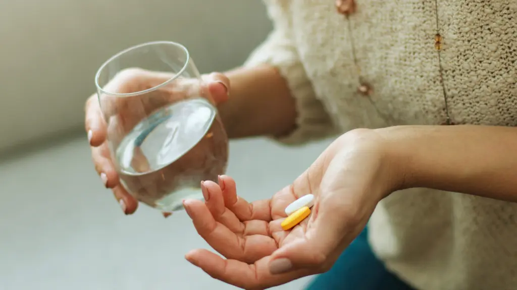 a woman holding supplements and a glass of water