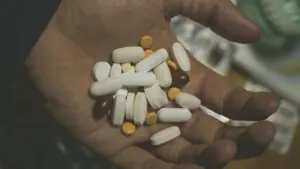 A hand holding a variety of dietary supplements, including capsules and tablets, in different shapes, sizes, and colors