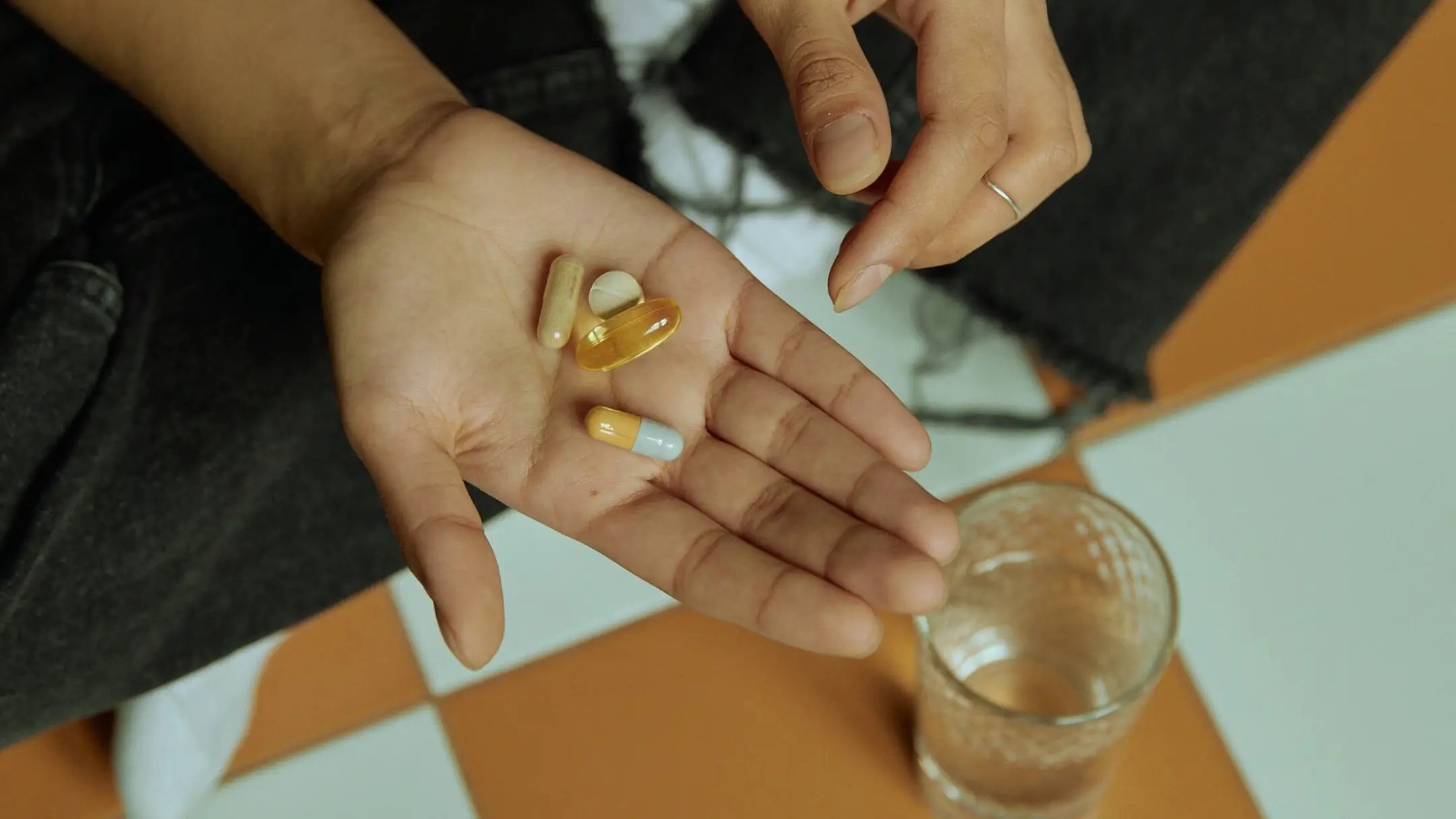 a woman holding supplements and a glass of water is on the table