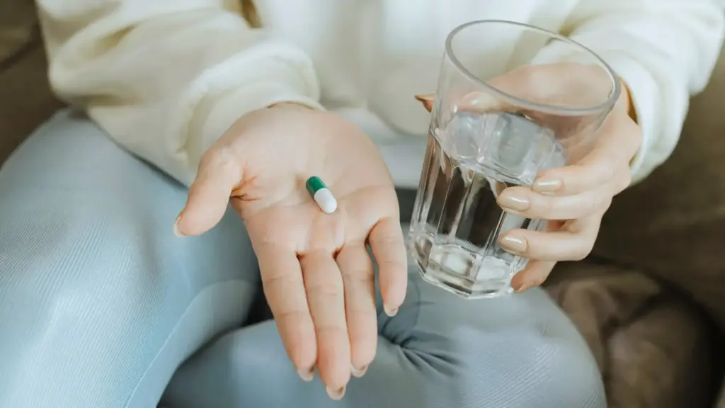 Woman holding a supplement capsule in one hand and a glass of water in the other