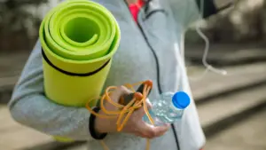 Active woman carrying a Pilates mat, jump rope, and water bottle outdoors